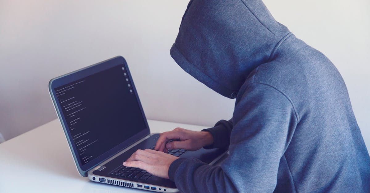 person in a hoodie hunched over an open laptop typing code