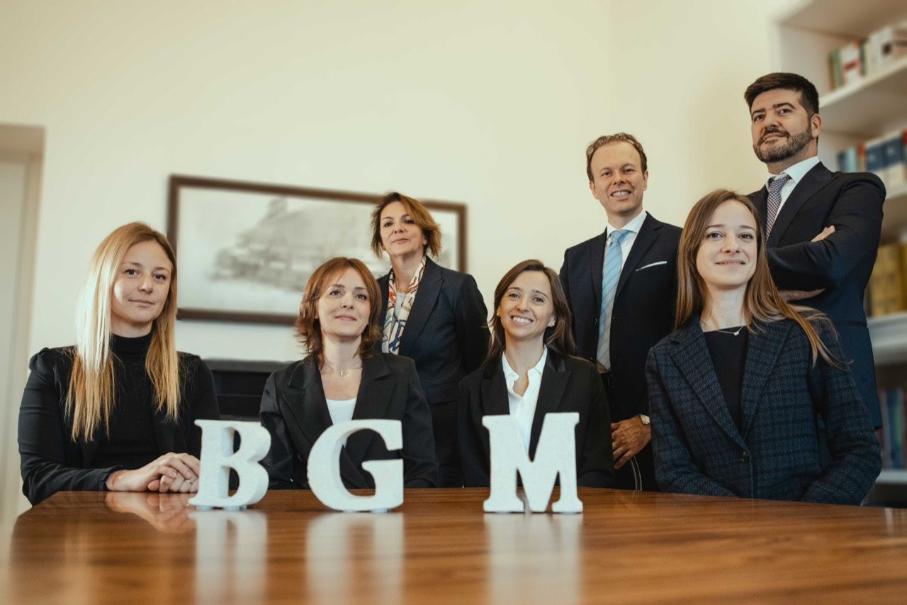 Un gruppo di persone in piedi attorno a un tavolo con sopra le lettere bgm.