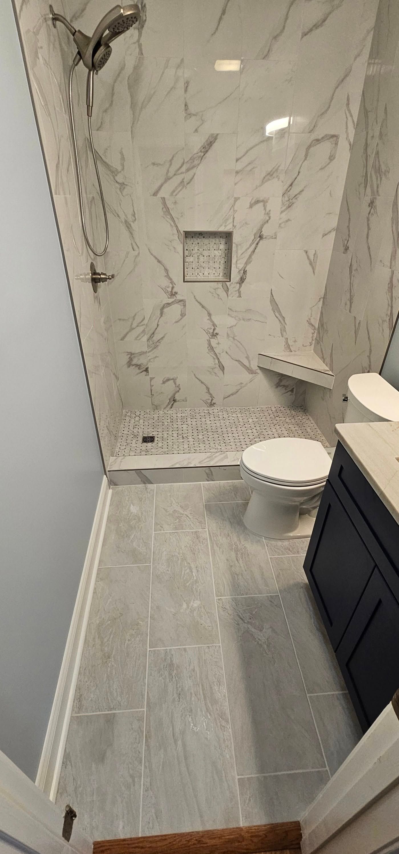 A small bathroom featuring a glass-enclosed shower with marble-look tile, gray floor tile, and a dark blue vanity.