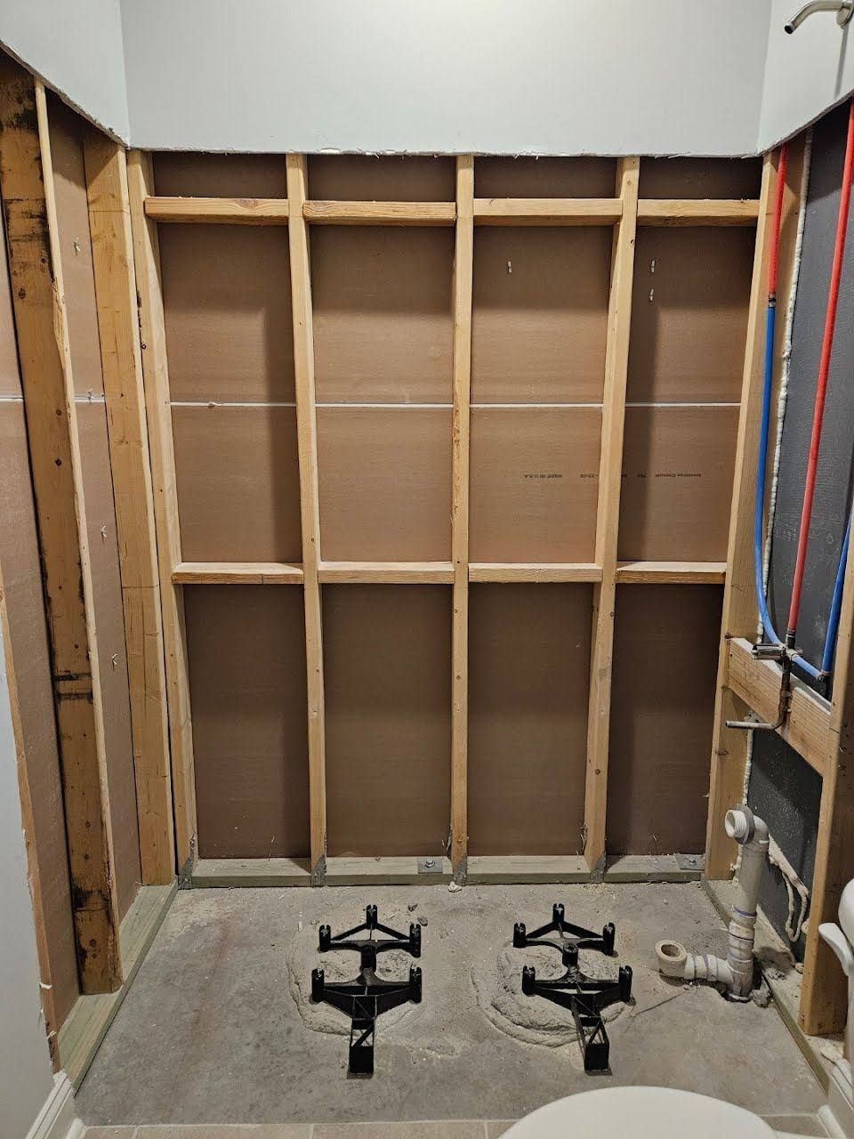 An unfinished bathroom renovation showing exposed wall studs and two metal shower drain bases set in a concrete floor.