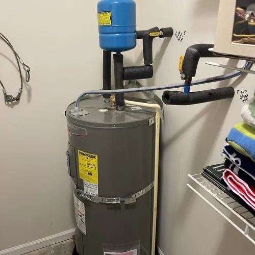 A gray water heater is sitting in a room next to a wall | The Duke Of Plumbing