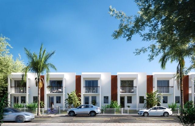 Modern white townhouses with balconies, parked cars, and palm trees under a blue sky