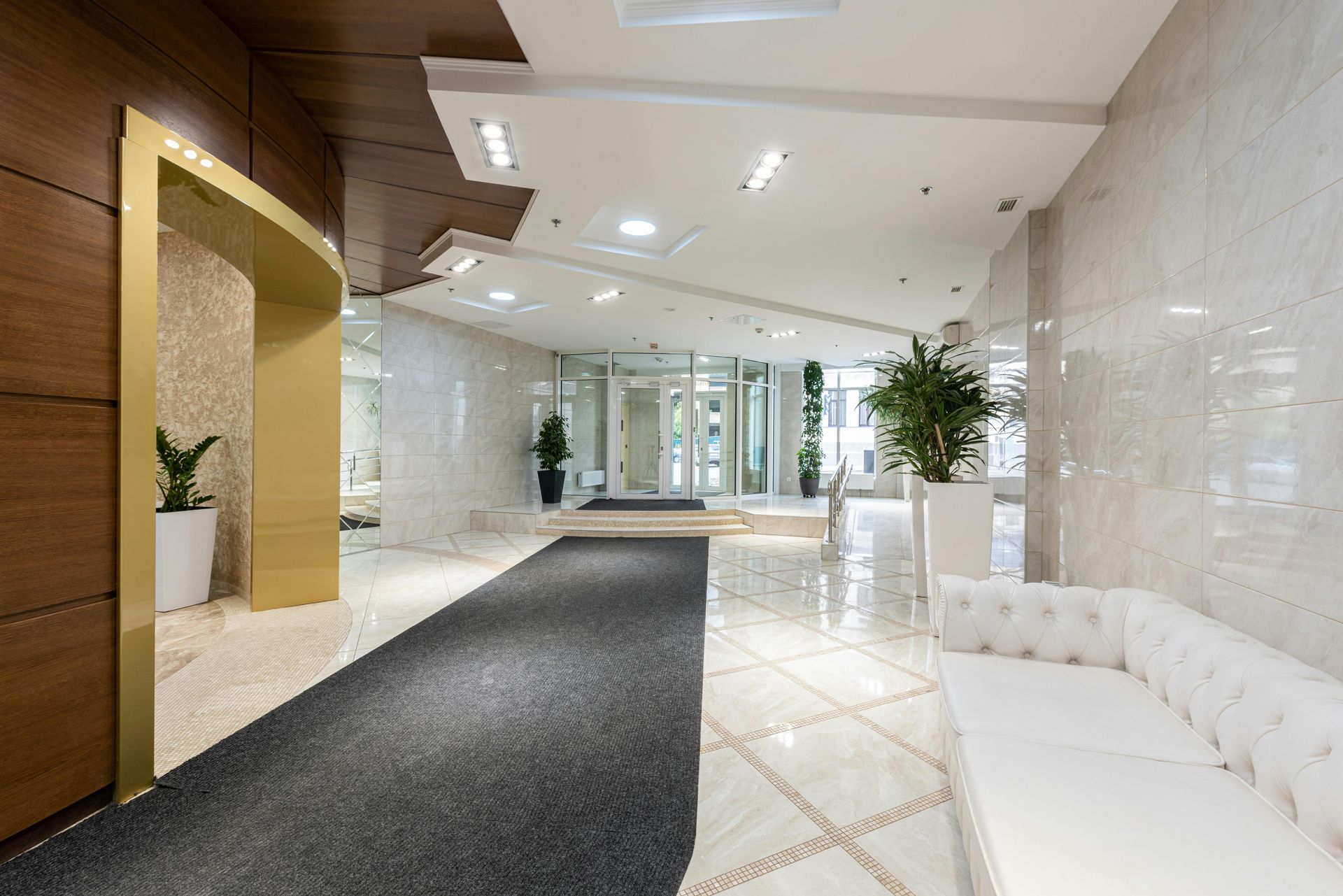 Modern hotel lobby with white marble floors, black runner, tufted bench, and plants