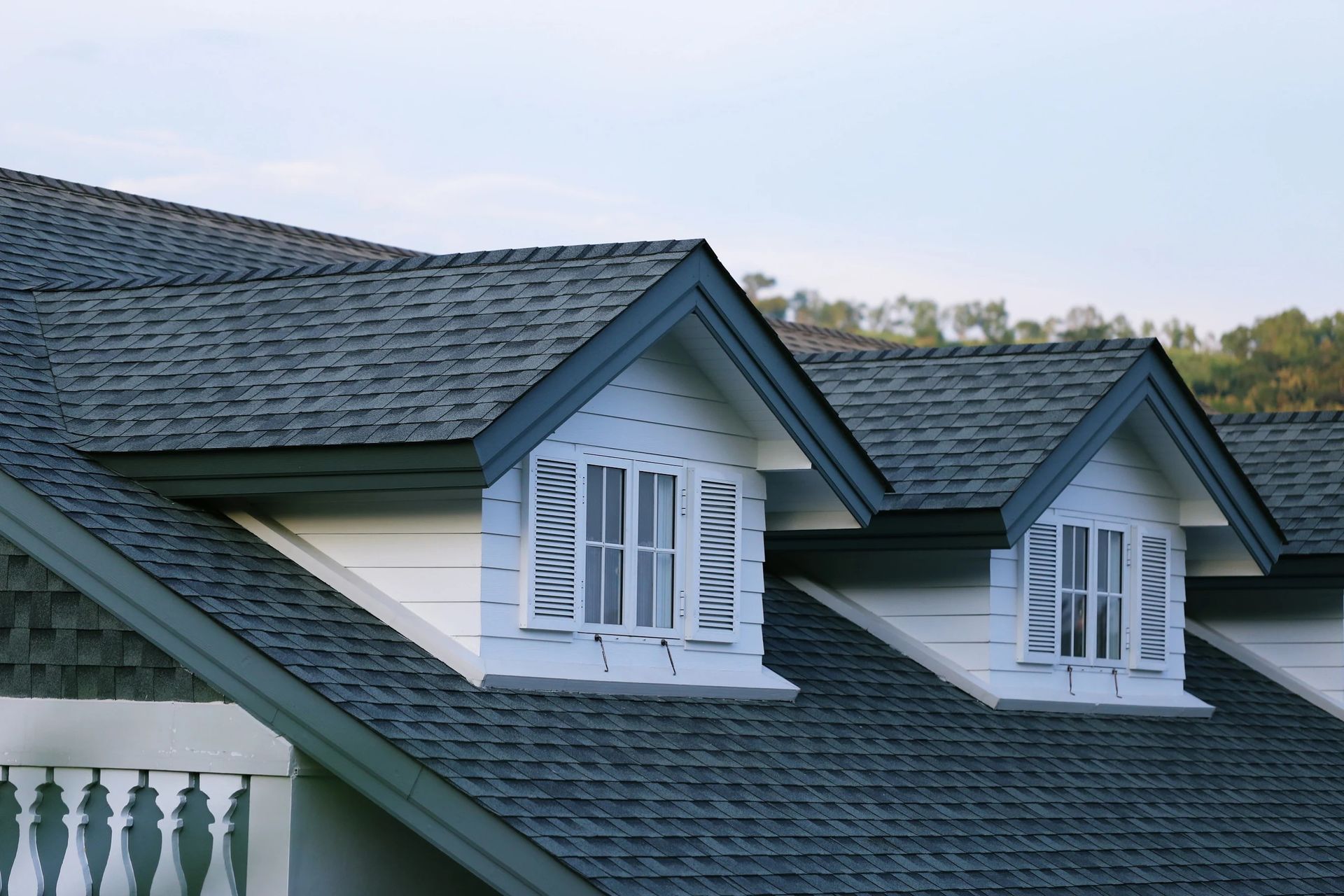 Gray shingled roof with three dormer windows, blue trim, white shutters.