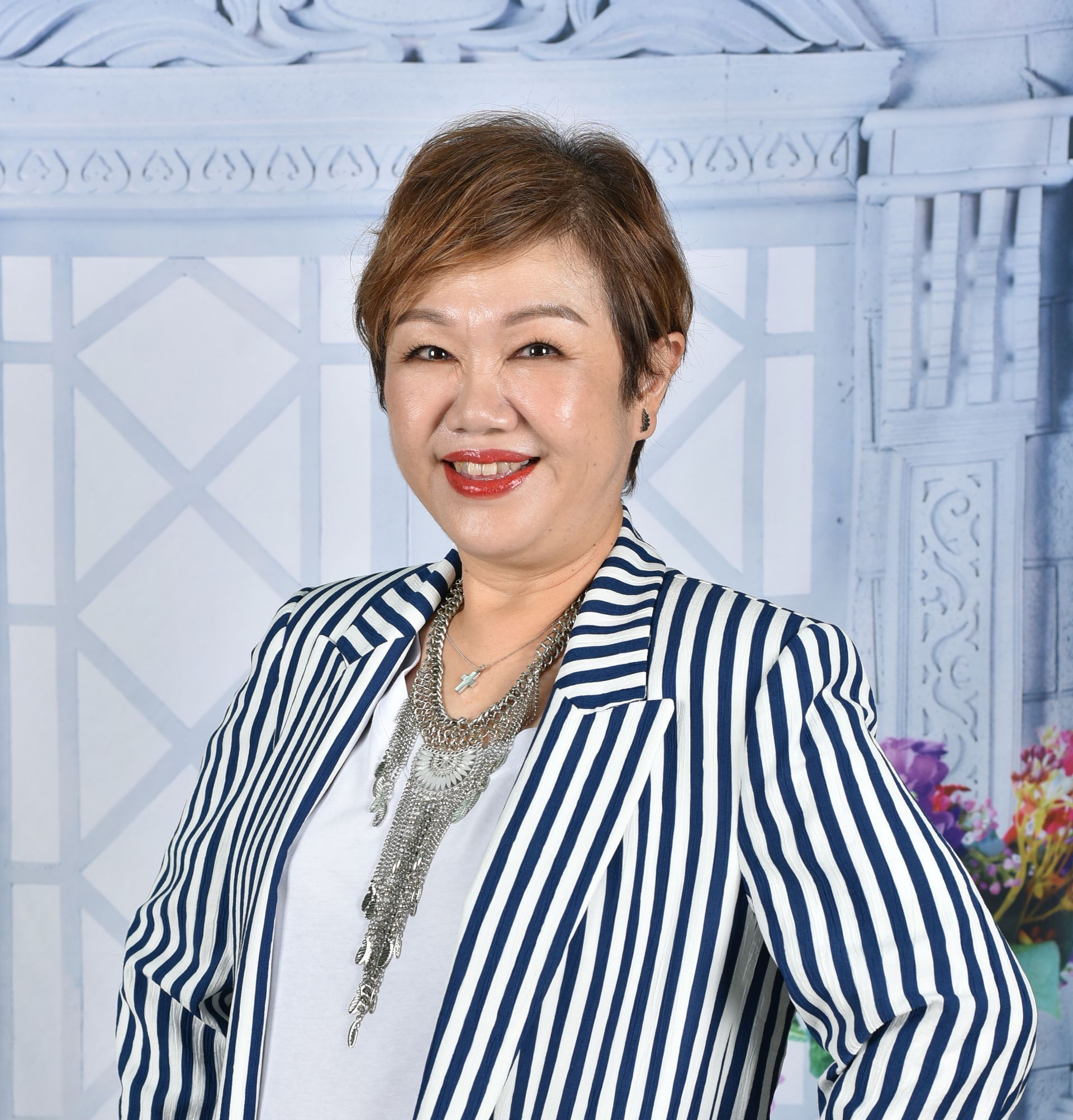 Woman in striped blazer smiling, standing in front of a decorative background with flowers.