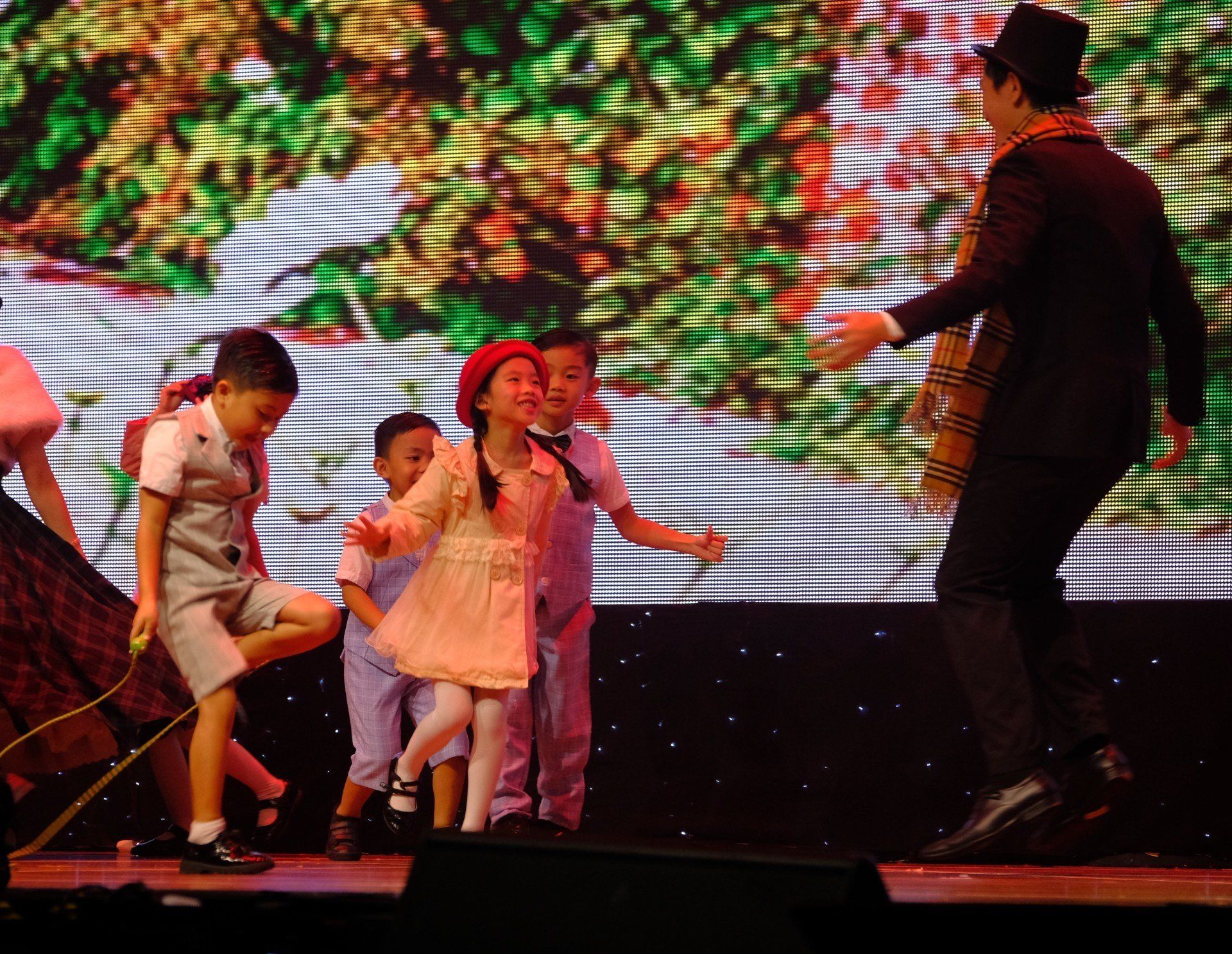 Children in costumes dancing on stage with a man in a top hat.