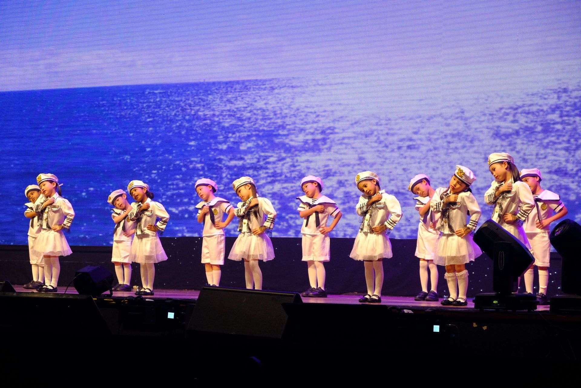 Children in sailor costumes performing on stage in front of a blue backdrop.