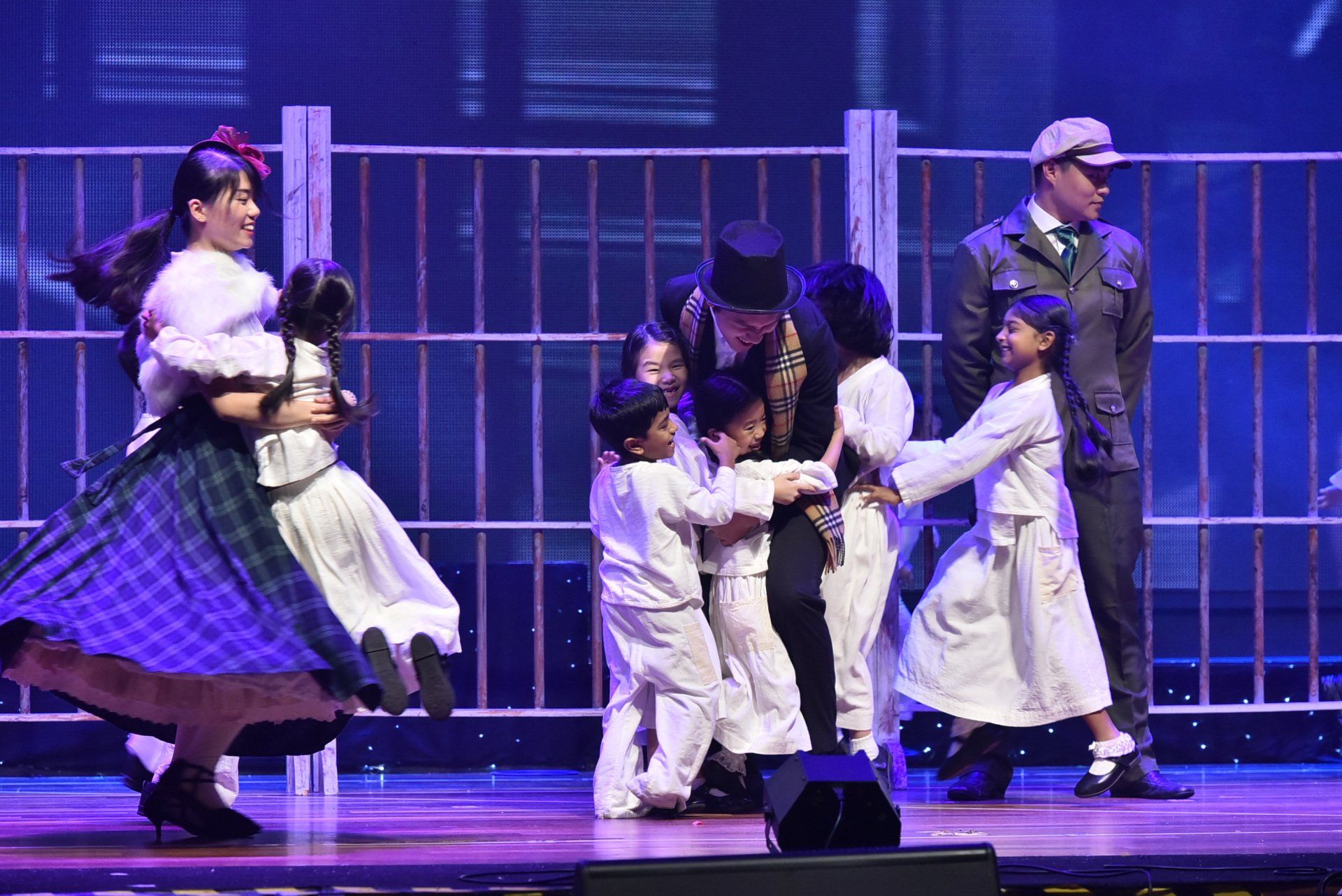 Stage performance with actors in period costumes: adults and children on stage, embracing.