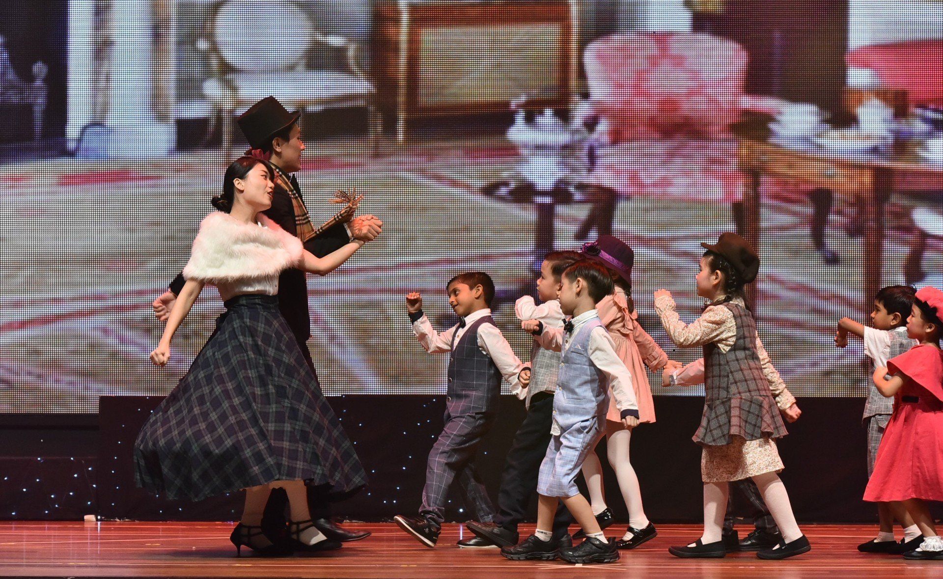 Children dancing on stage with two adults in period costumes.