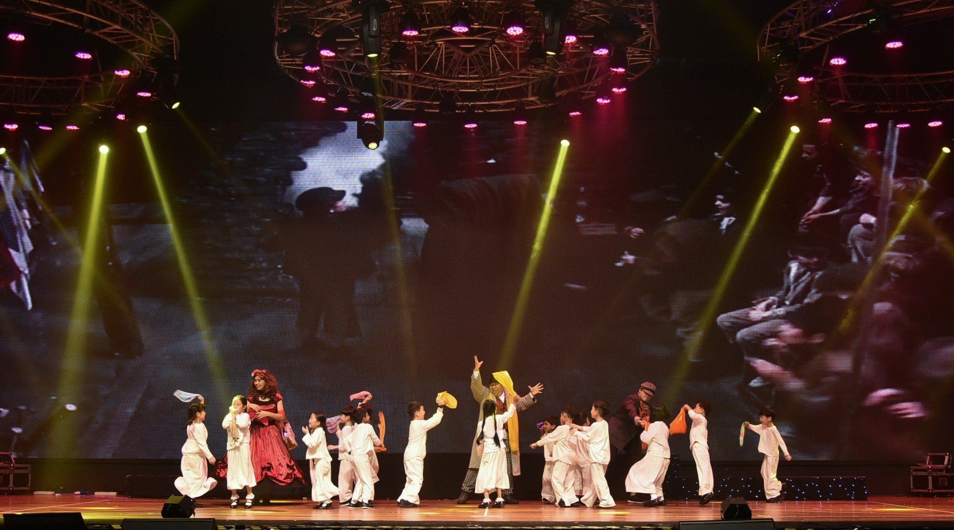 Stage performance with dancers in white and yellow costumes, under yellow spotlights.