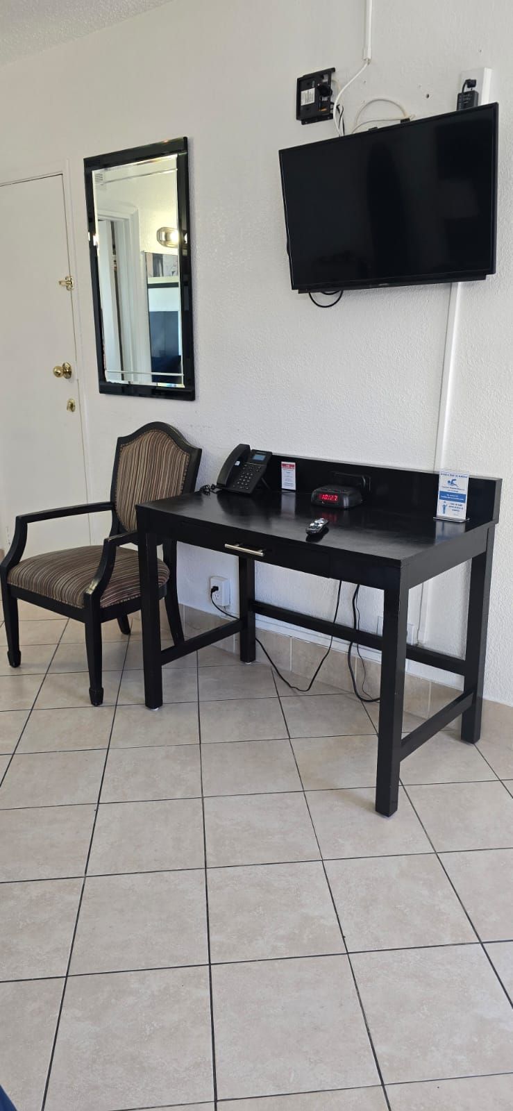 A room with a desk , chair , television and mirror.