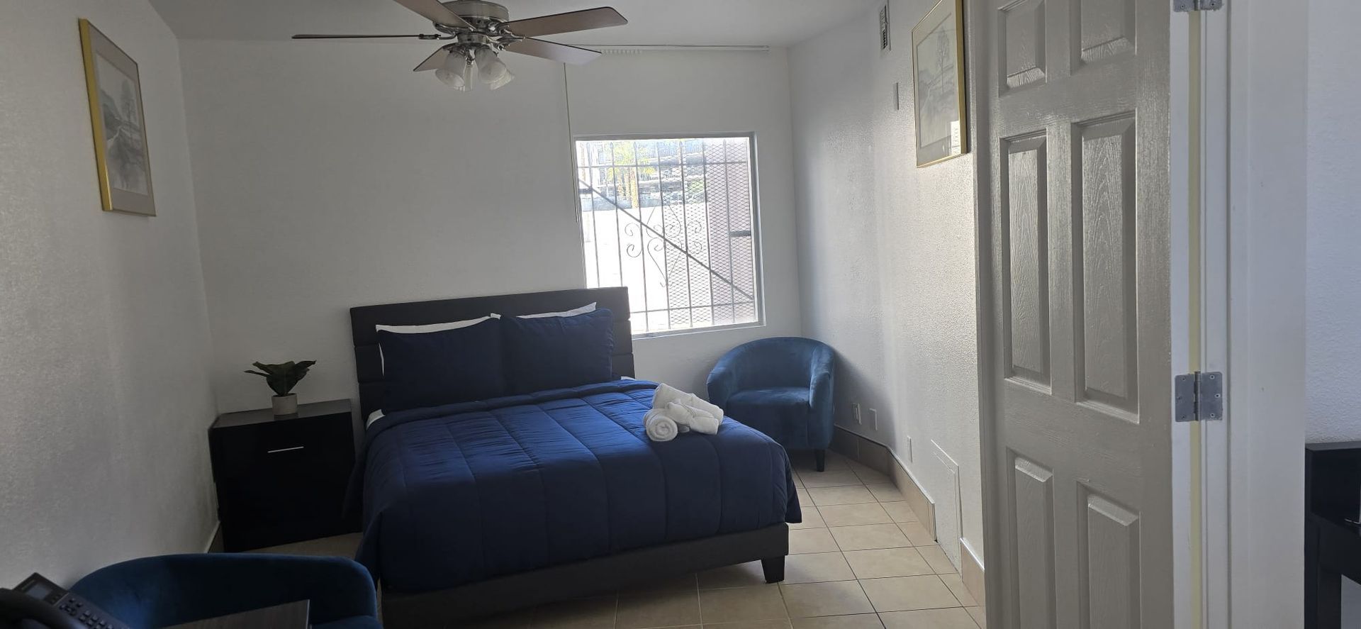 A bedroom with a bed , chairs , nightstand and ceiling fan.