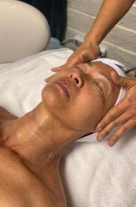 A woman is laying on a bed getting a massage on her face.