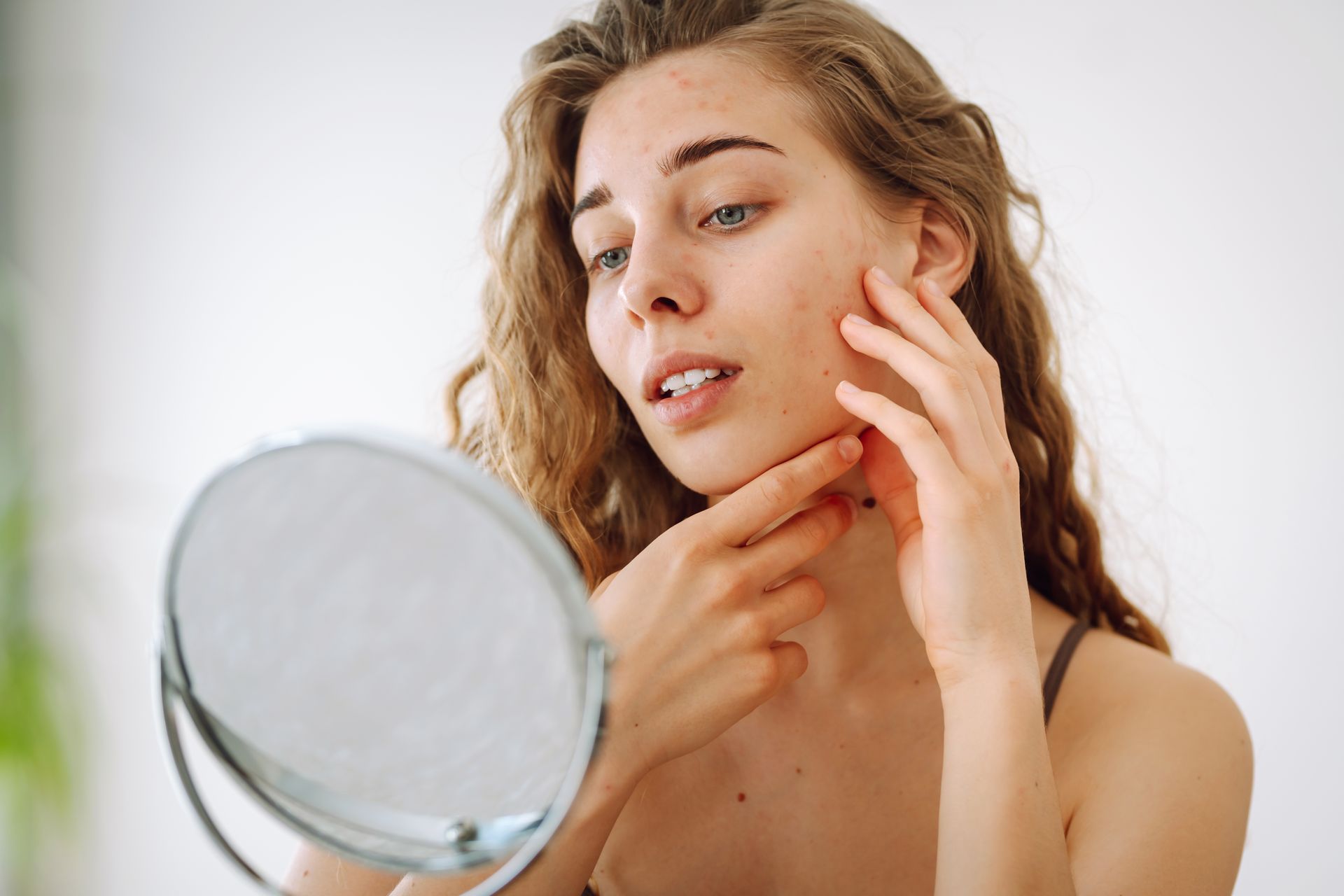 A woman is looking at her face in a mirror.