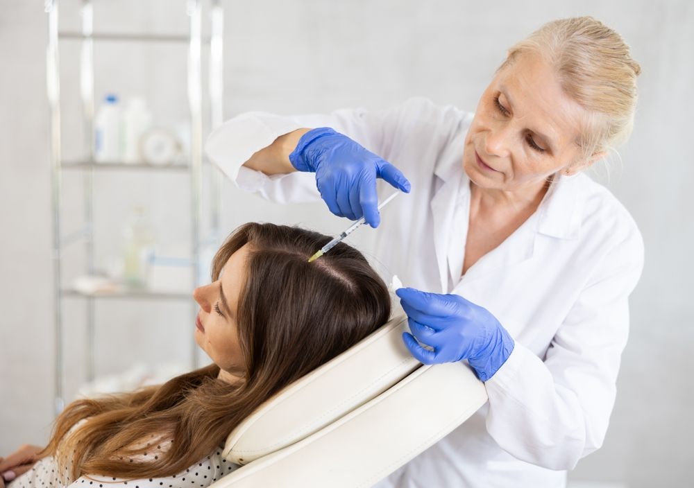 A woman is getting an injection in her hair by a doctor.