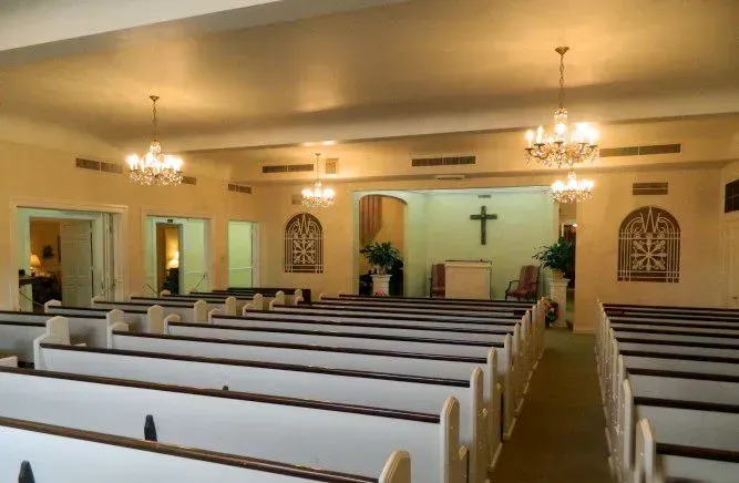 Empty church interior with rows of pews, chandeliers, and a cross on the front wall