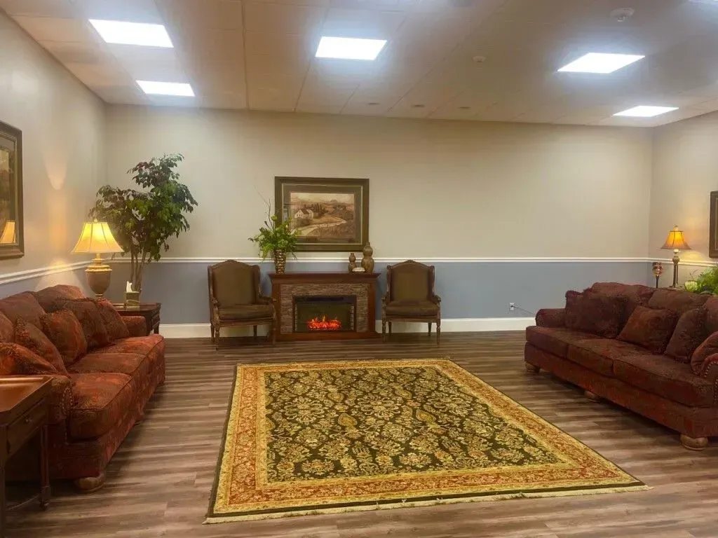 Spacious living room with patterned rug, brown sofas, fireplace, potted plant, and soft lamps.