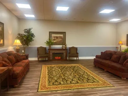 Spacious living room with patterned rug, brown sofas, fireplace, potted plant, and soft lamps.