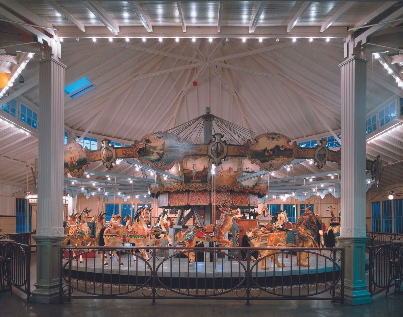 Indoor carousel with colorful horses and riders under a bright white canopy