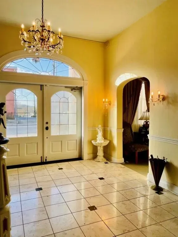 Elegant foyer with yellow walls, chandelier, arched doors, tiled floor, and curtained doorway.