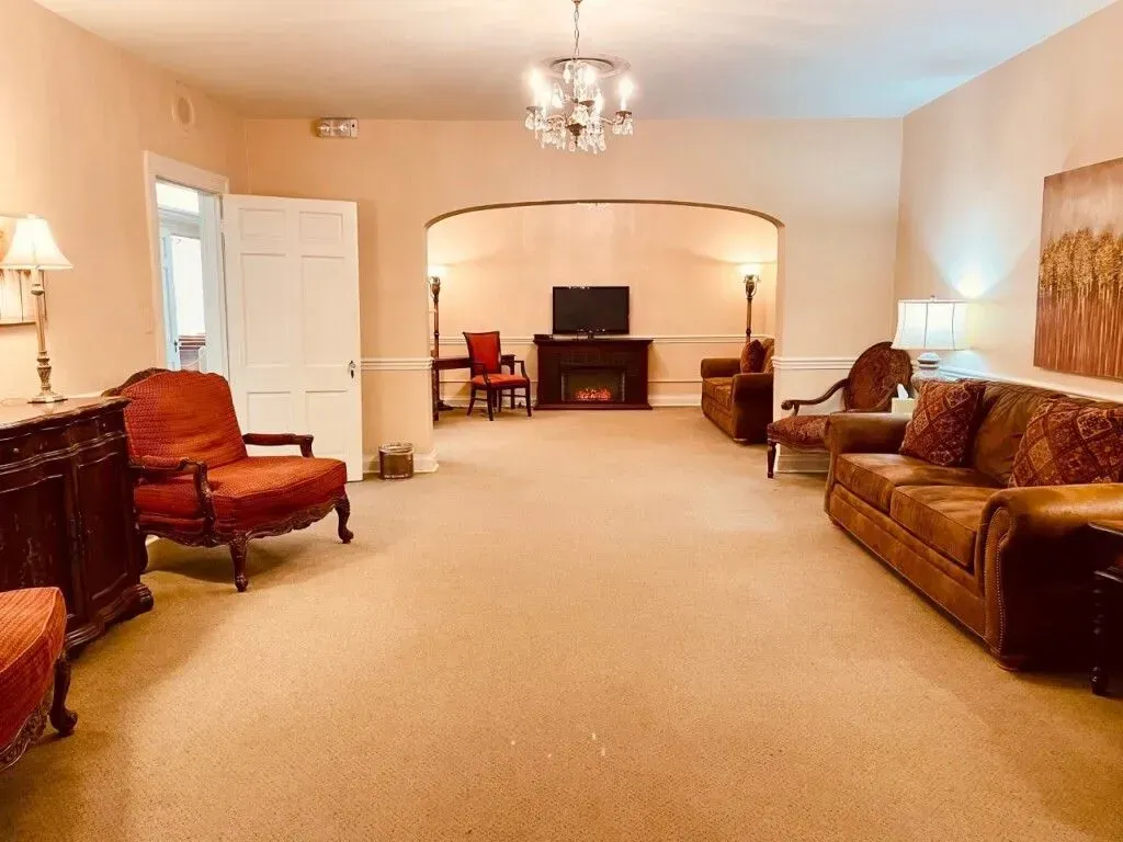 Spacious beige living room with sofa, armchairs, chandelier, and TV on a console against the back wall