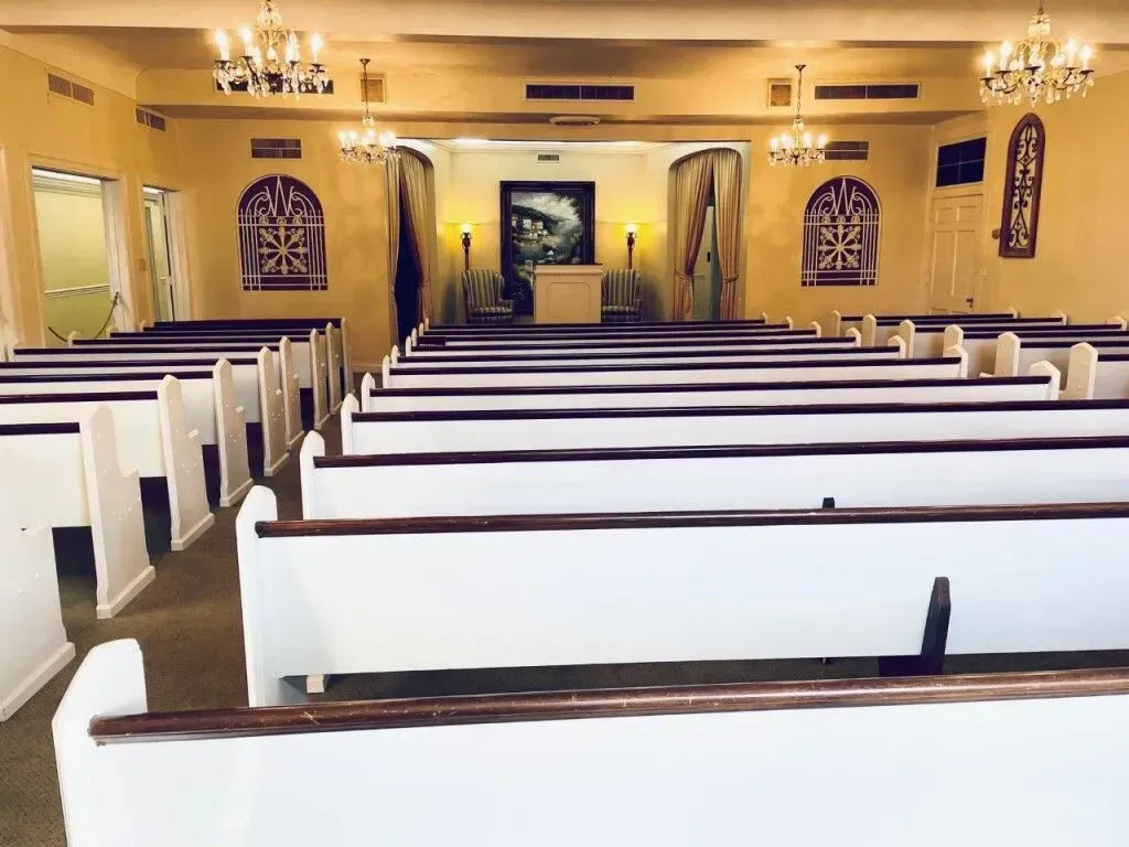 Empty church sanctuary with rows of white pews, chandeliers, and a central aisle facing the altar