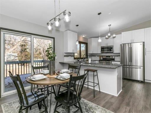 A dining room with a table and chairs and a kitchen with stainless steel appliances.