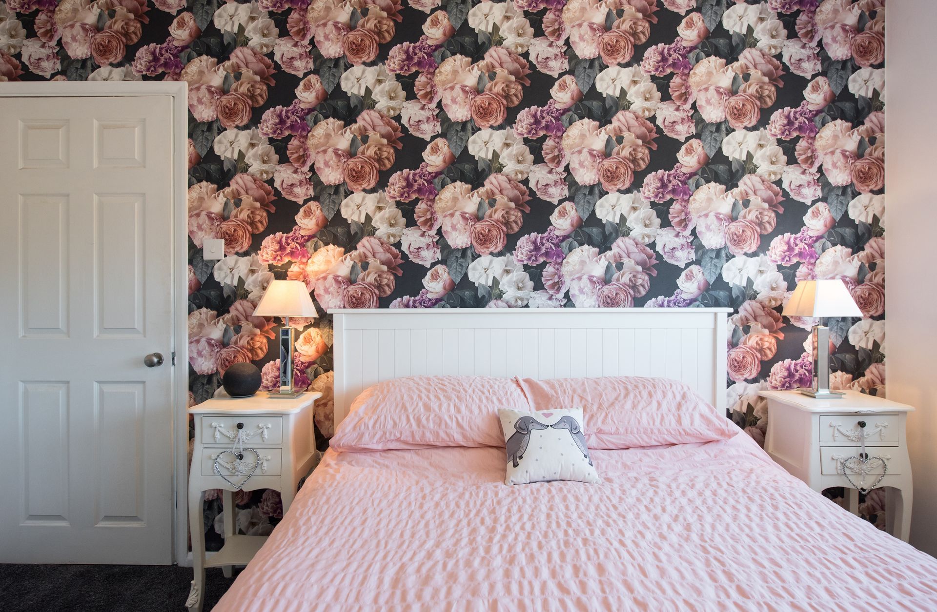 A bedroom with a bed , nightstands , and a floral wallpaper on the wall.
