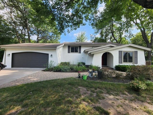 A white house with a black garage door is surrounded by trees.