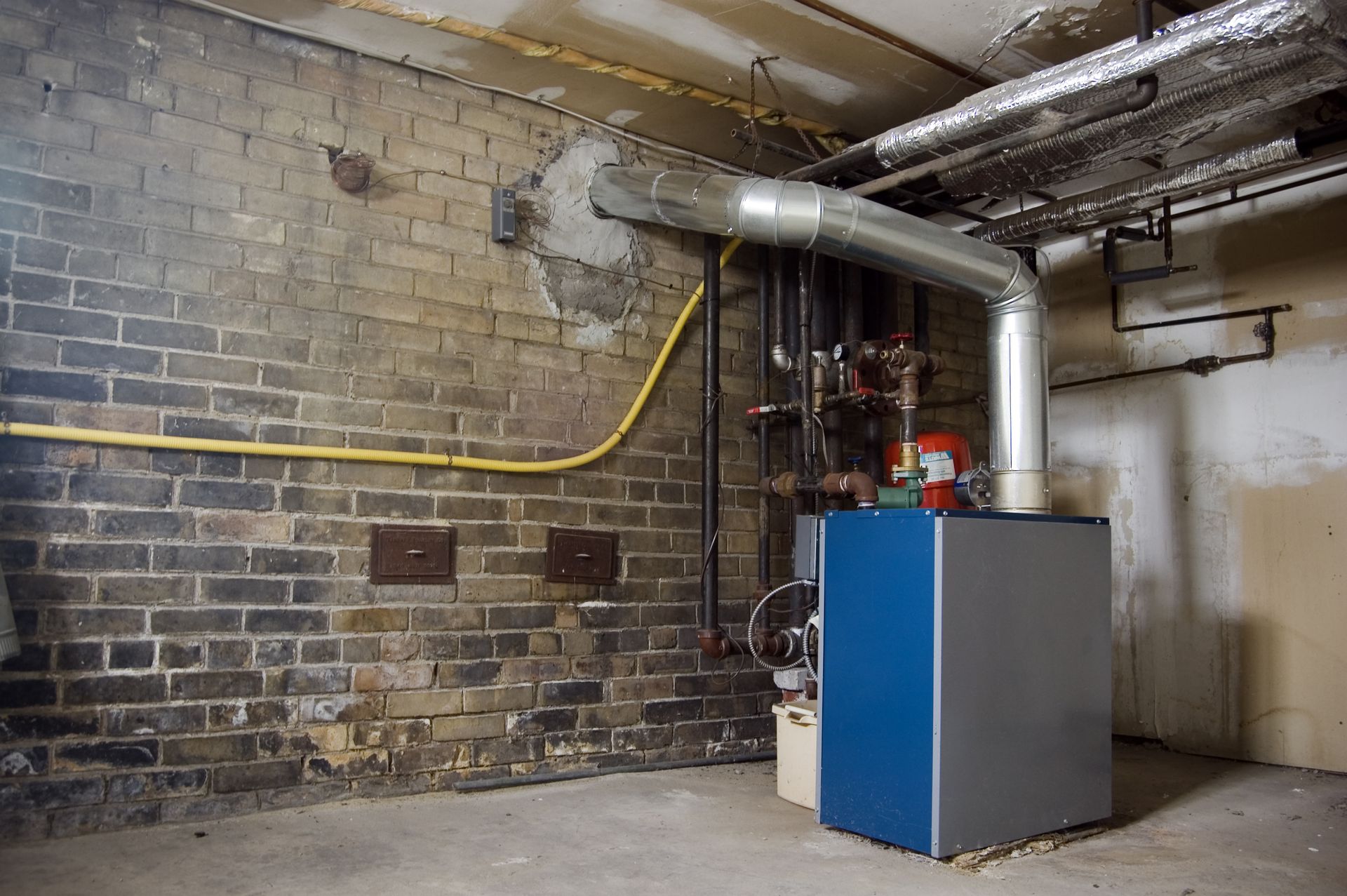 A blue boiler is sitting in a basement next to a brick wall.