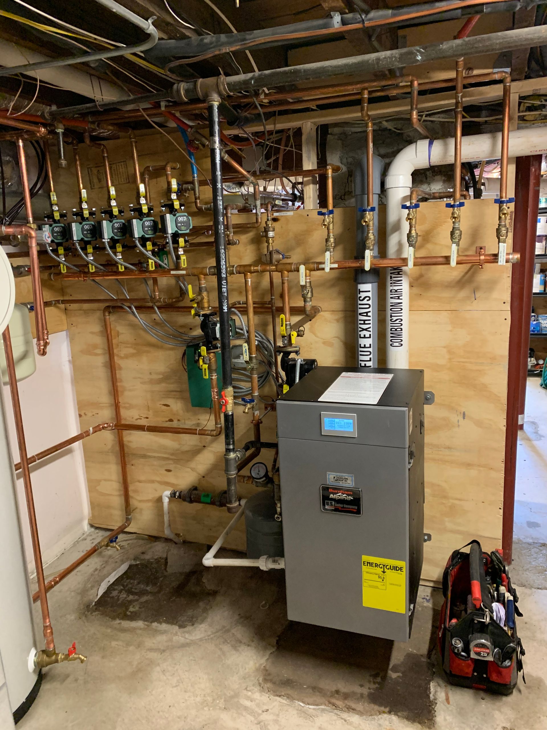 A boiler is sitting in a basement next to a water heater.