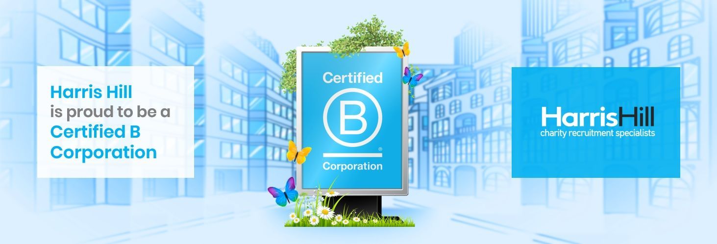 Harris Hill Certified B Corporation. Sign with the logo, background buildings, blue color scheme, and green foliage.