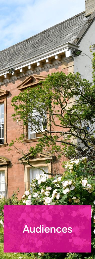 A brick building with white trim, trees, and a pink button with the word 