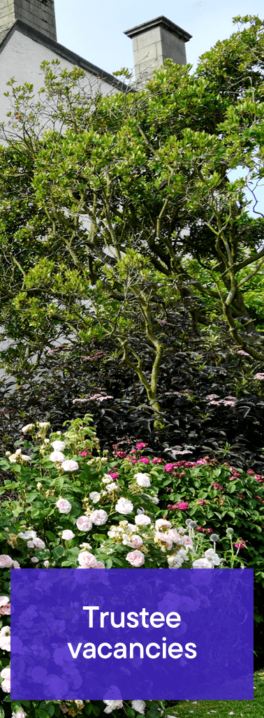 View of a building with a chimney surrounded by greenery. A sign with 