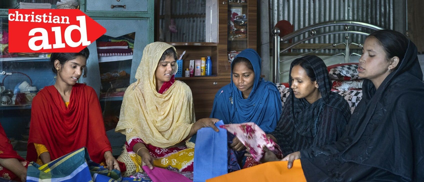 Five women looking at fabric in a room, with a Christian Aid logo.