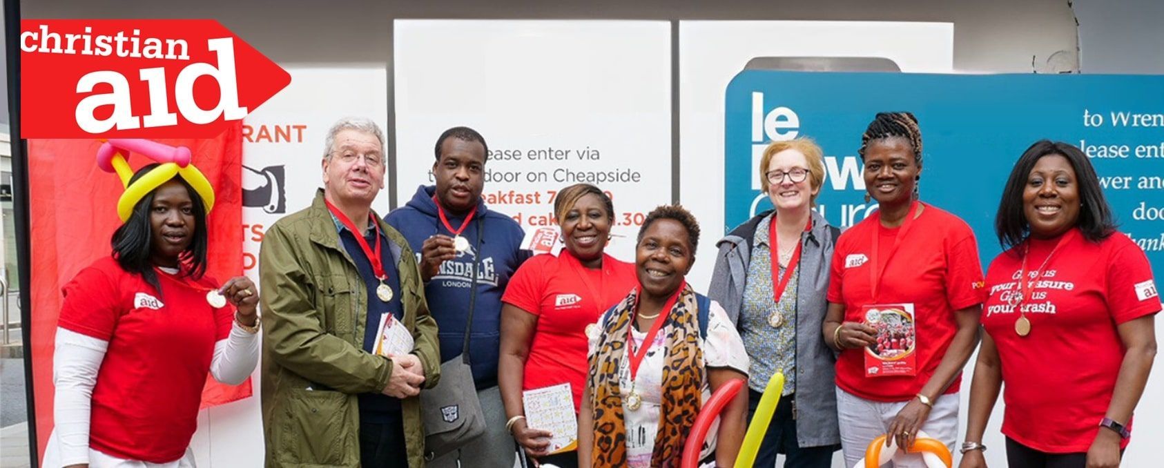 Group of people in red shirts and medals posing next to a Christian Aid sign.