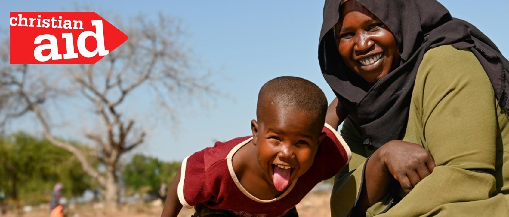 A woman and a child smiling together outdoors. The child has his tongue out. Christian Aid logo.