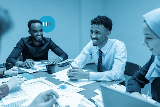 Group of people in business attire at a table, smiling while looking at documents. Blue-toned.