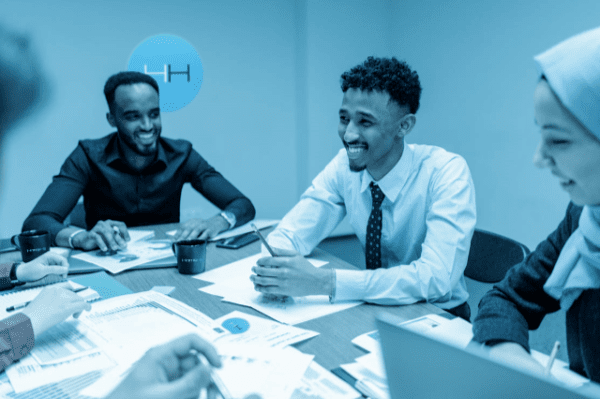 People smiling during a meeting, at a table with papers, in a blue-lit office.