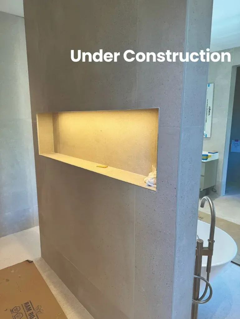 Interior wall under construction with recessed shelf, warm lighting, and a partially visible bathroom.