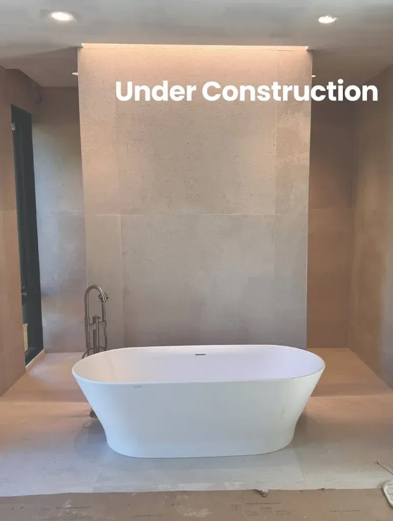 Bathroom under construction with a white freestanding bathtub and chrome faucet. Beige walls.