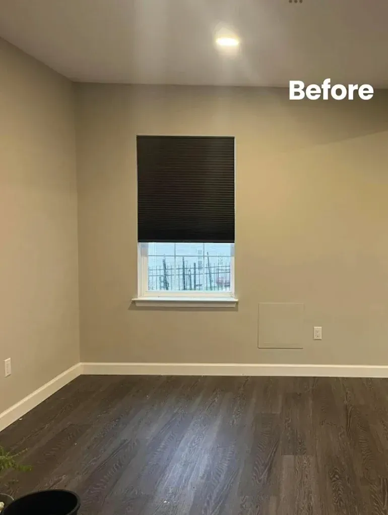 Empty room with dark wood floors, tan walls, window with black shade. 