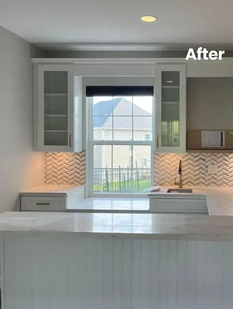 White kitchen with cabinets, window, and backsplash. The countertop is in front of the window.