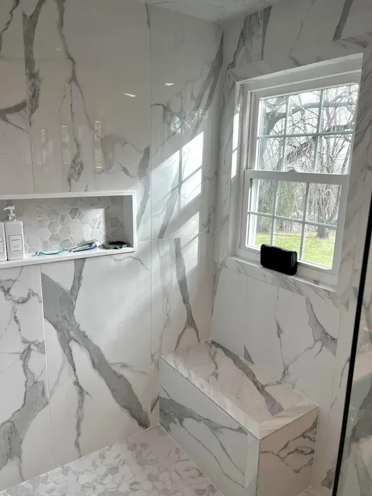 White marble tiled shower with a window, built-in seat, and shelf.