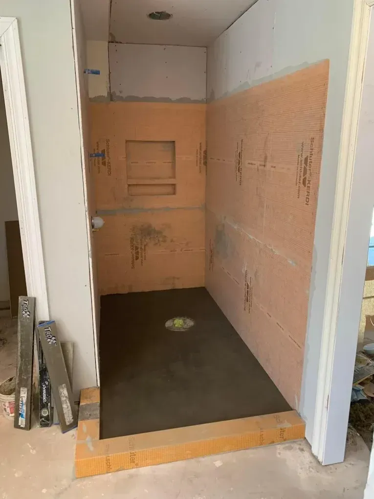 Shower stall under construction, orange walls and floor, gray concrete floor, rectangular niche.