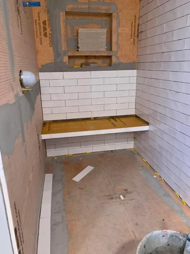 Shower stall under construction, with tiled walls, built-in bench, and a recessed shelf.