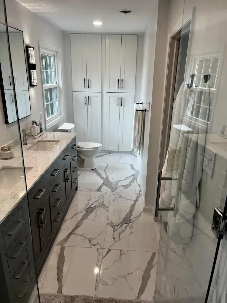 Modern bathroom with a long marble floor, white cabinets, and a gray double vanity.
