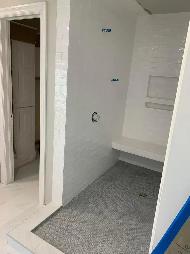 Shower with white walls and gray tile floor, featuring a built-in bench and niche.