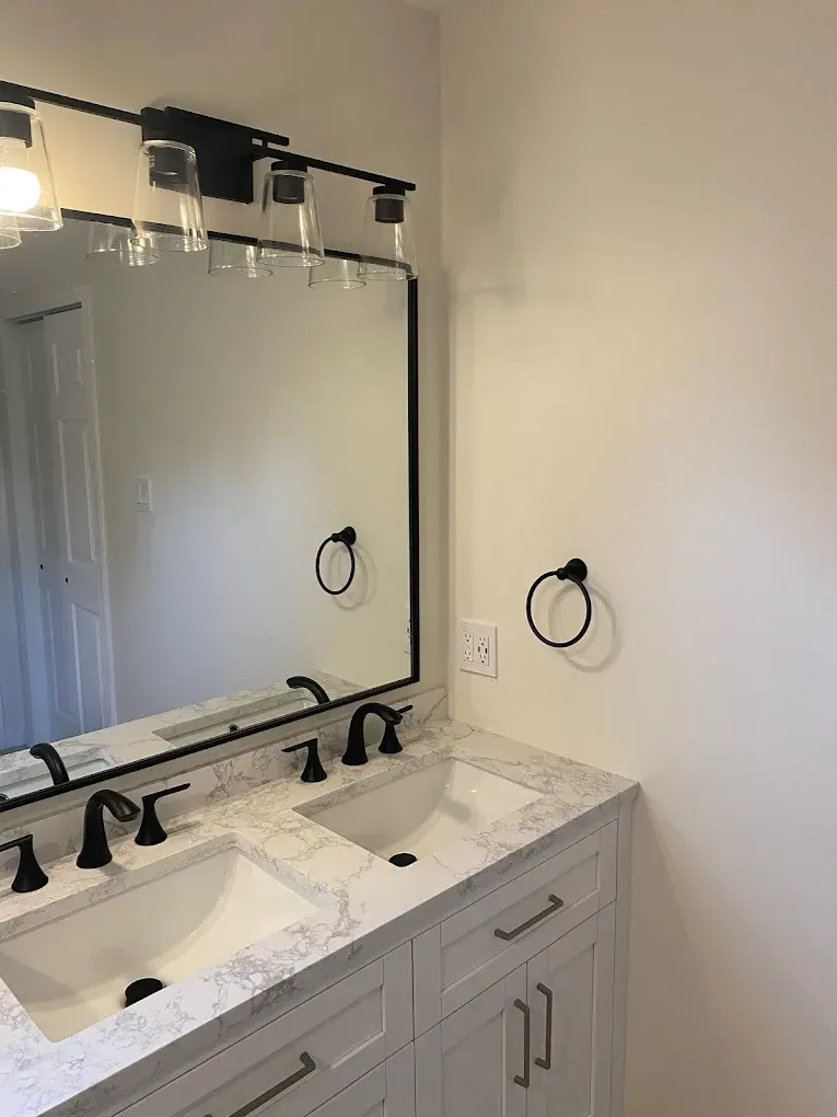 Bathroom with white double vanity, marble countertop, black fixtures, and a large mirror.