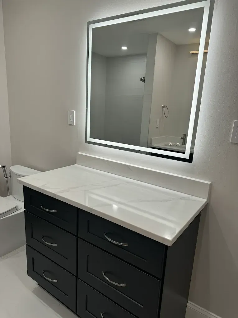 Bathroom vanity with a black cabinet, white countertop, and illuminated mirror.